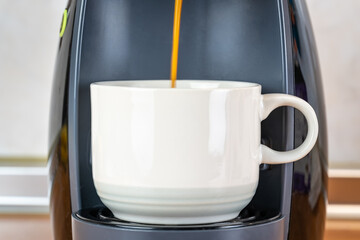 Cup of white pocelain in an automatic coffee maker while the coffee comes out freshly made.