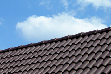 sloped dark brown clay tile roof and ridge. construction, modern building materials and technology concept. blue sky and fluffy white cloud. bright summer light. low angle abstract view 