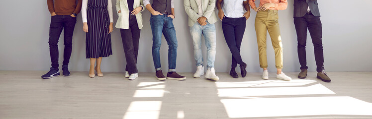 Fototapeta na wymiar Banner with diverse fashion models posing in studio. Group of multiethnic business people in smart casual outfits standing on floor by office wall. Cropped low section shot of men's and women's legs