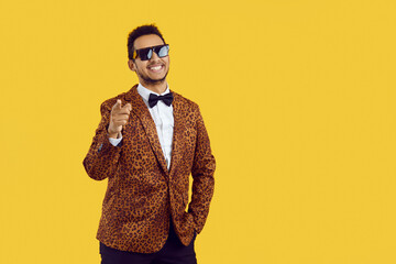 Portrait of smiling young African American man in animal print jacket isolated on yellow studio background. Happy black fashionable male point at camera screen. Copy space. Style and fashion.
