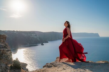 A woman in a red flying dress fluttering in the wind, against the backdrop of the sea.