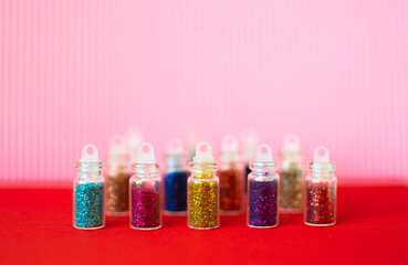 Lots of round jars with colorful bright sequins on a pink background. Sparkling sequins. Shiny products in transparent bottles, close-up. Selective focus