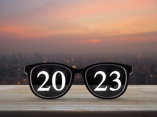 2023 white text with black eye glasses on wooden table over blur of cityscape on warm light sundown, Business vision happy new year 2023 cover concept