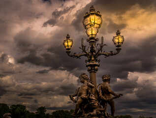 old Parisian lamp post illuminated in front of a cloudy sky