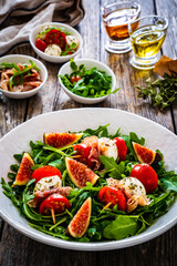 Fresh salad - mozzarella, crudo ham, fig, cherry tomatoes and leafy greens on wooden table
