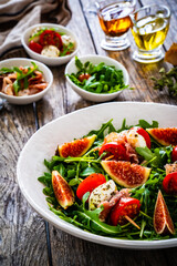 Fresh salad - mozzarella, crudo ham, fig, cherry tomatoes and leafy greens on wooden table
