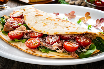 Italian piada wraps - piadina stuffed with fresh vegetable leaves, parmesan and prosciutto crudo on wooden table
