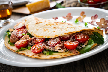 Italian piada wraps - piadina stuffed with fresh vegetable leaves, parmesan and prosciutto crudo on wooden table
