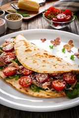 Italian piada wraps - piadina stuffed with fresh vegetable leaves, parmesan and prosciutto crudo on wooden table
