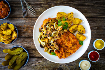 Breaded fried pork chop with fried potatoes and mushrooms on wooden table
