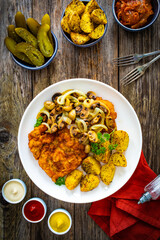 Breaded fried pork chop with fried potatoes and mushrooms on wooden table
