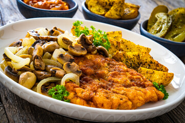 Breaded fried pork chop with fried potatoes and mushrooms on wooden table

