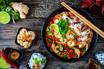 Tom Yum - Thai soup with prawns and rice noodles on black wooden table
