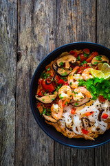Tom Yum - Thai soup with prawns and rice noodles on black wooden table
