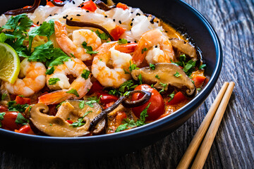 Tom Yum - Thai soup with prawns and rice noodles on black wooden table
