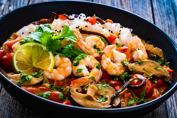 Tom Yum - Thai soup with prawns and rice noodles on black wooden table

