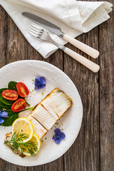 Fish dish - fried halibut with lemon and fresh vegetables on wooden table
