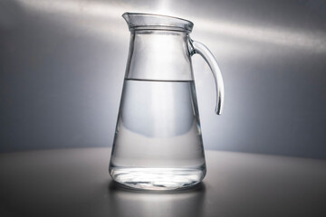 A glass decanter filled with clean drinking water beautifully illuminated on a gray background....