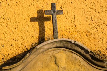 Cross on a tombstone at a yellow wall