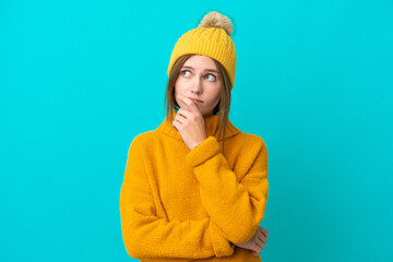 Young English woman wearing winter jacket isolated on blue background having doubts and with...