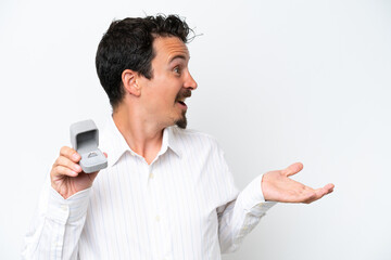 Young man holding a engagement ring isolated on white background with surprise facial expression