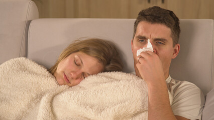 CLOSE UP: Cute couple with a seasonal cold resting under blanket and watching TV