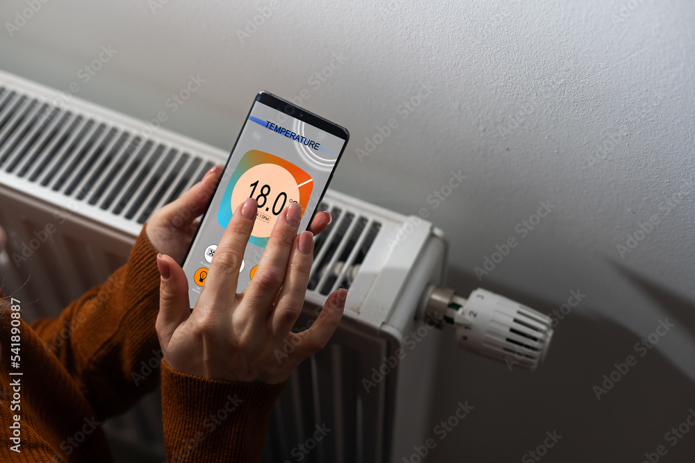 Poster close-up of person hand setting temperature of thermostat using mobilephone at home