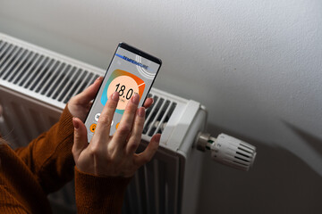 Close-up Of Person Hand Setting Temperature Of Thermostat Using Mobilephone At Home