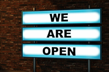 We are open. Black letters on a light box. The illuminated sign placed in front of a brick wall. Shopping, reopening and retail concept. 3D illustration