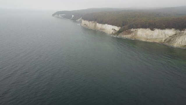 flyby drone shot of the Jasmund national park cliffs with its UNESCO world heritage beech forests in misty October weather