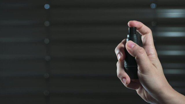Closeup of a person holding a black perfume vaporizer and spraying it into the air