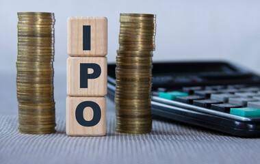 IPO - acronym on wooden cubes on the background of coins and calculator