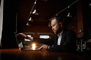 A focused bearded businessman working in an internet cafe on his laptop.