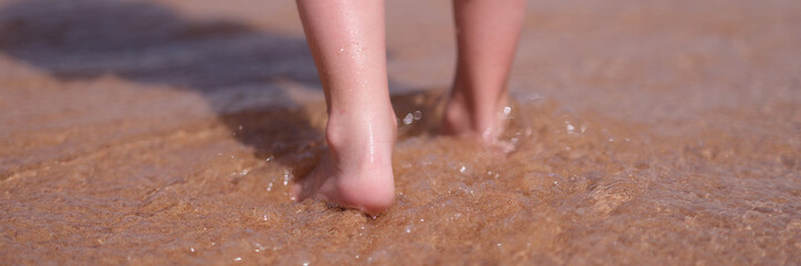 Fototapeta premium Bare feet of child walking along sea shore closeup