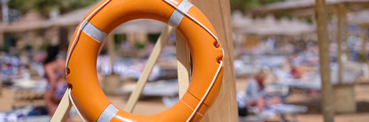 Orange lifebuoy weighing on hotel beach closeup