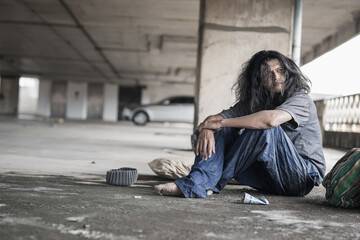 Homeless people sit on the streets in the shadows of buildings and ask for help and money the troubles of the big modern city. - obrazy, fototapety, plakaty