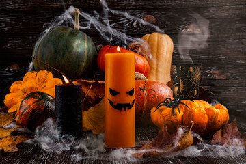Halloween pumpkins, spiders, web and autumn leaves. An orange candle with a scary face and dark candles as decor. Festive composition on a dark background.