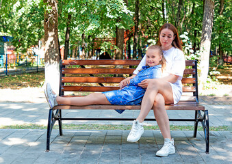 Mother and daughter sitting on a bench in the park. Outside on a sunny day