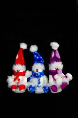 Three handmade toy snowmen with hats and scarves on a black background. Made of felt, scarf, black button, close up. Decor. Christmas and New Year concept