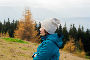 young pretty girl smiling enjoys rest in a hat and jacket against the background of yellow autumn pine trees forest modrina needles in the Carpathians mountains