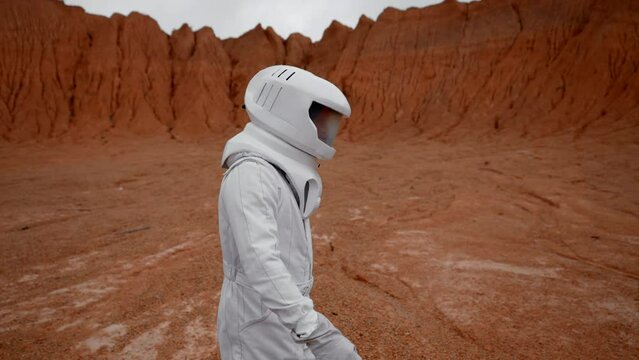 Astronaut walking at Mars crater surface. Sideview in slow motion of lonely man in cosmic costume exploring new territory for Earth relocation.