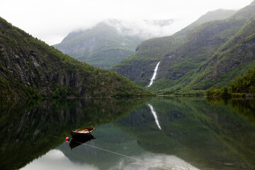 Fototapeta na wymiar Rowboat on a lake with waterfall reflection, Norway