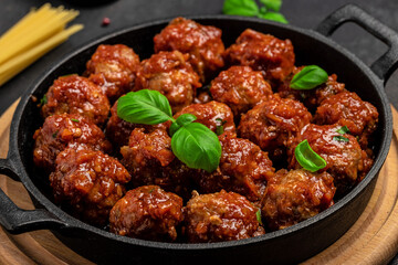 Meatballs in sweet and sour tomato sauce. in frying pan on dark background