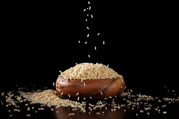 Brown long grain rice pouring into a wooden bowl on a black background. Part of the cereal woke up...
