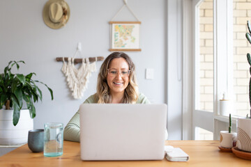 Smiling woman working from home on laptop at kitchen table