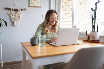 Smiling woman working from home on laptop at kitchen table