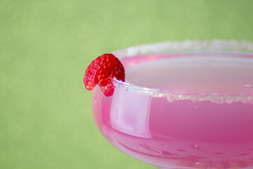 pink raspberry cocktail on a green background with raspberries and accessories for its preparation