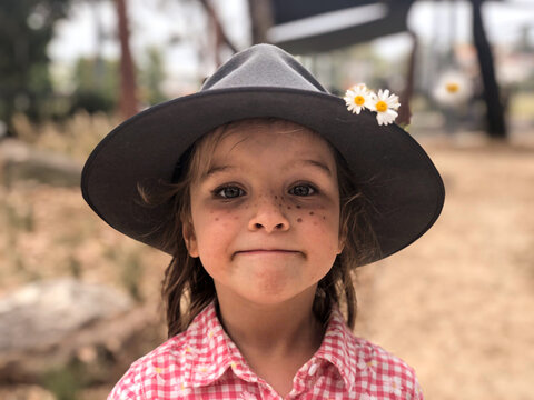 Close up shot of a smiling girl wearing a hat with two daisy flowers