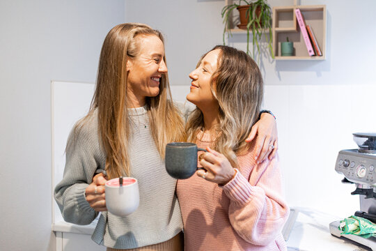 Happy female same sex couple standing together, looking at one another with coffees