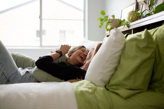 Female same sex couple  affectionately lying together on the bed, hugging and laughing together